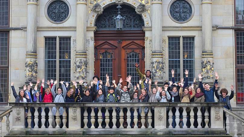 A group of international students stand in front of the entrance to Bremen City Hall. They all seem relaxed.