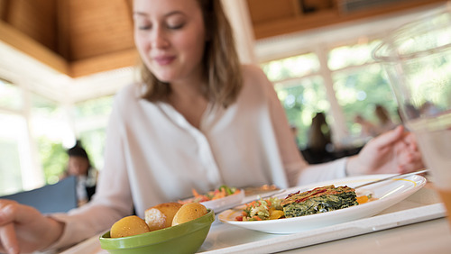 Eiene Person sitzt in der Mensa, vor ihr steht ein Tablett mit Essen