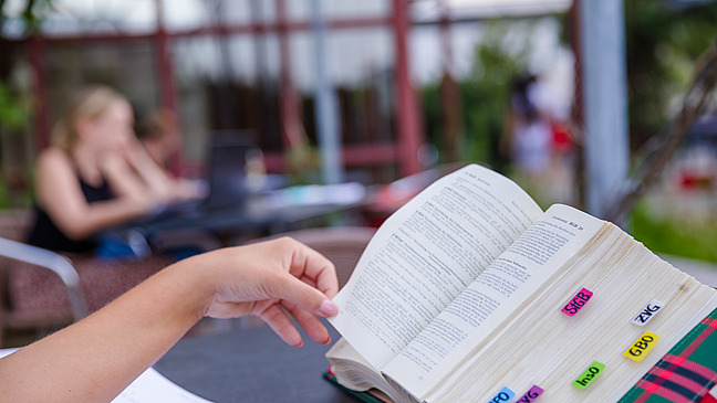 Close-up of a book being leafed through by a person. It has many colorful bookmarks.