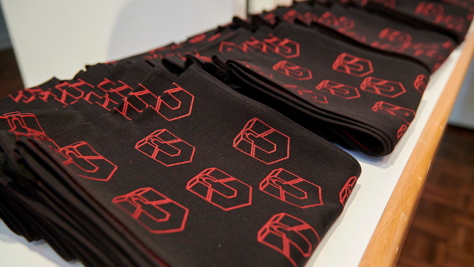 Nahaufnahme von einer Reihe gefalteter Schals. Sie sind schwarz und rot bestickt mit einem Logo, das eine Kombination aus dem Buchstaben U und dem Torbogen eines historischen Gebäudes darstellt.