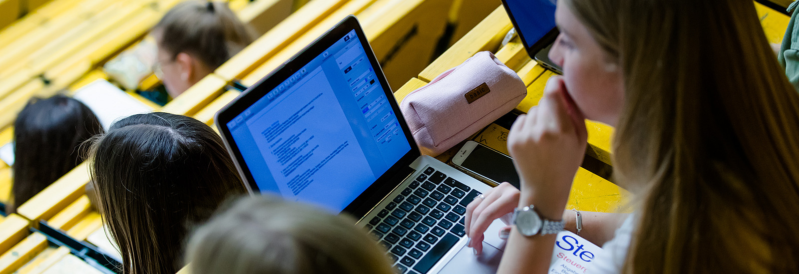 Two female students in a lecture hall. One of them has a laptop.