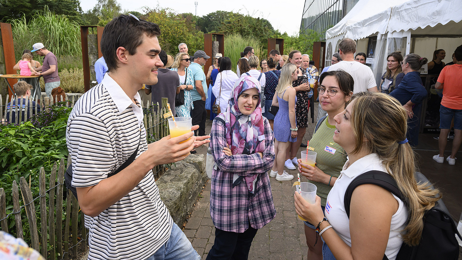 Mehrere fröhliche Personen mit Getränken bei einer Gartenparty.