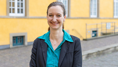 Eine Frau in einem schwarzen Blazer lächelt in die Kamera.