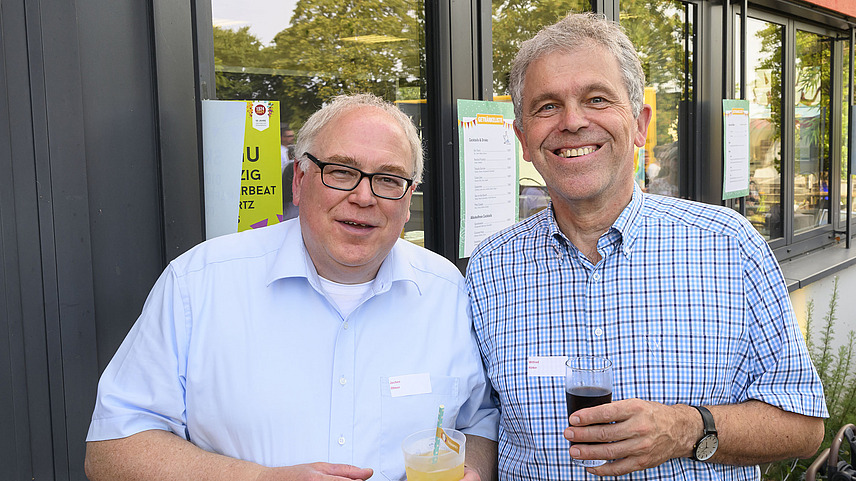 Two men with drinks laugh at the camera.