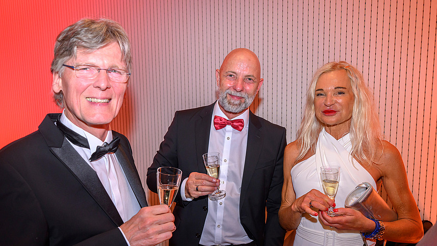 Three people with champagne glasses smile into the camera