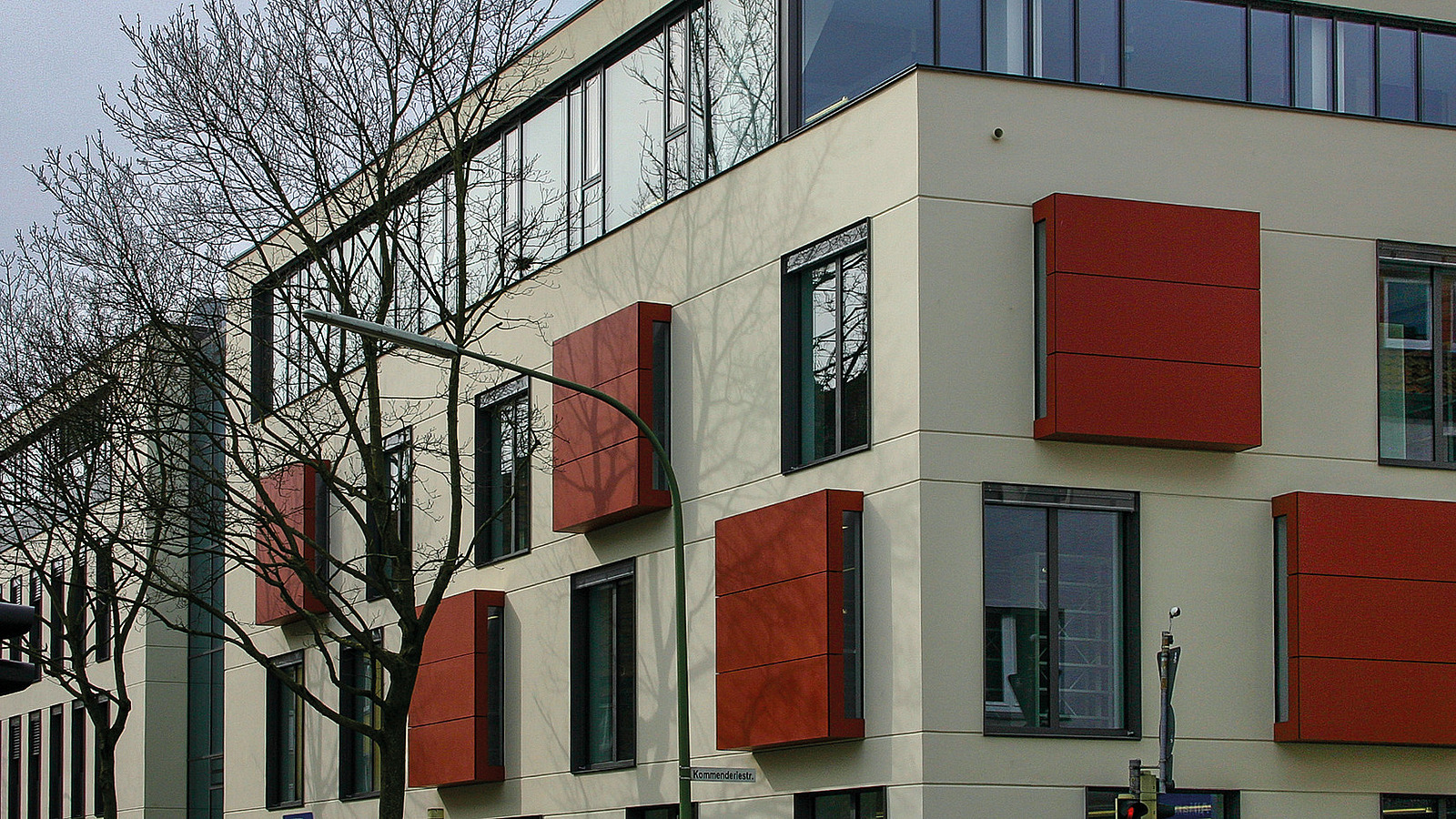 Farbfoto mit einem Blick auf die Fensterfassade des Gebäudes. Einige der Fenster haben eine dunkelrote Verkleidung.