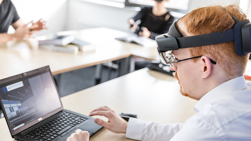 A person sits in front of a laptop wearing an augmented reality headset