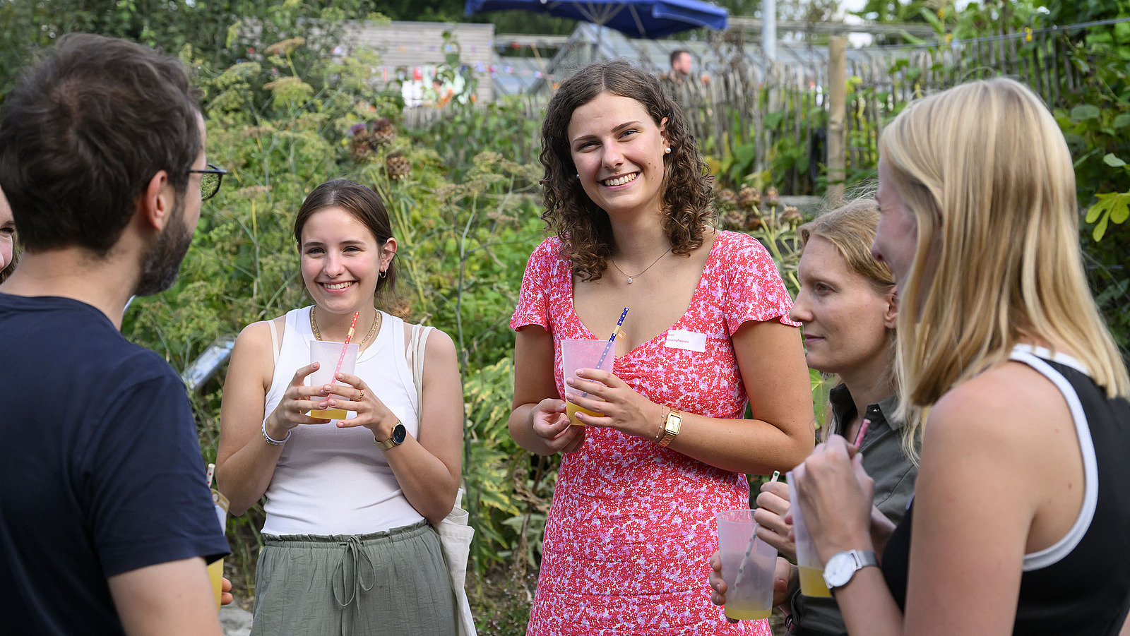 Mehrere fröhliche Personen mit Getränken bei einer Gartenparty.