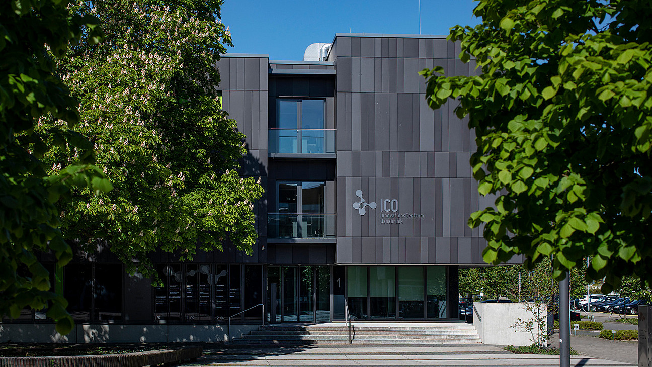 Ein Eingang in das Innovationscentrum Osnabrück zwischen zwei Bäumen.