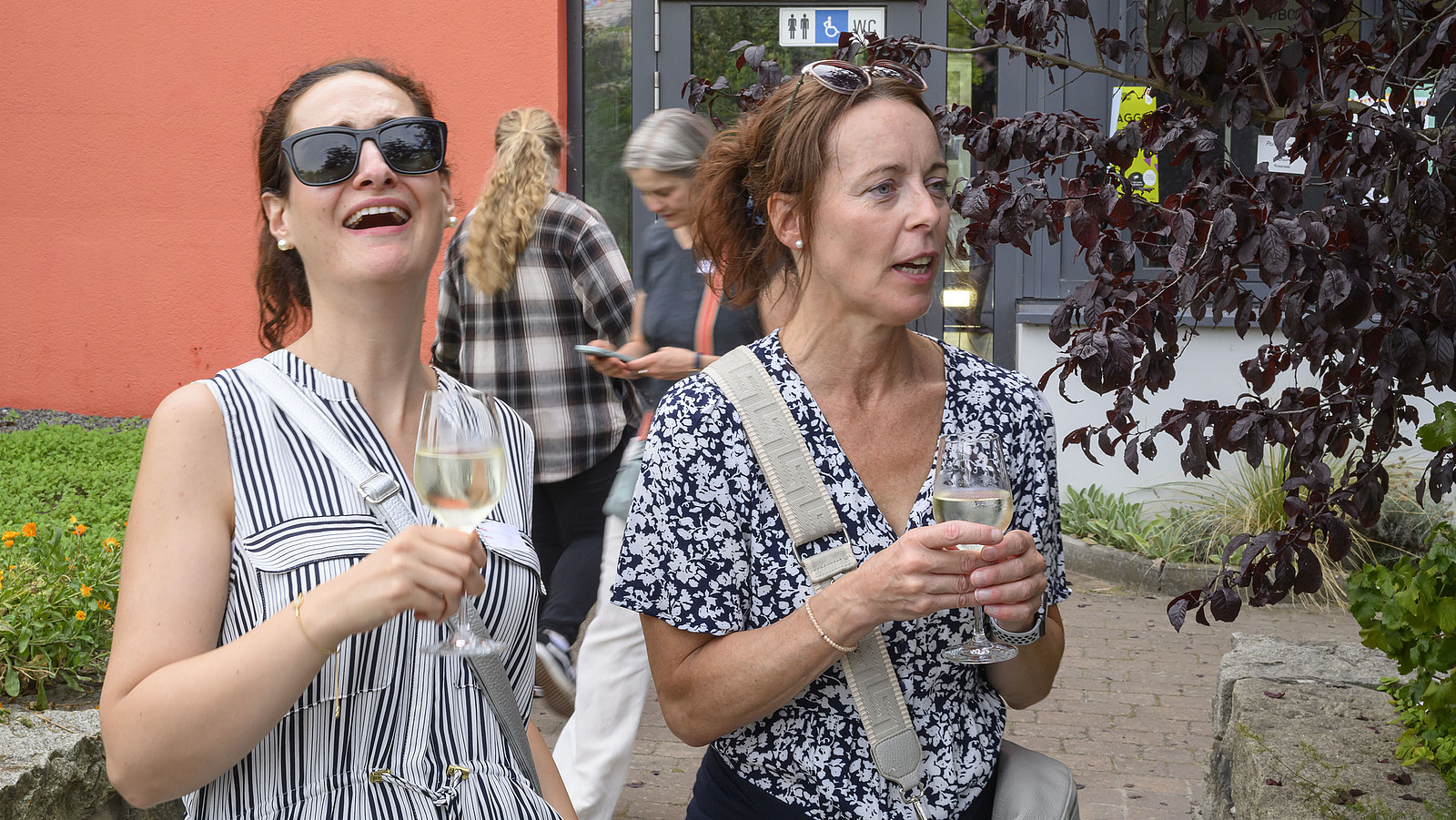 Zwei lachende Frauen mit Getränken in der Hand.