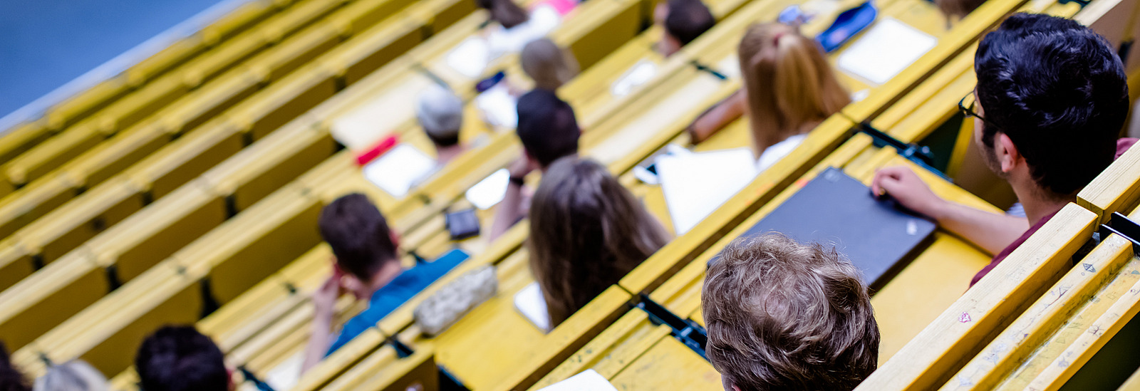 View from above of rows of seats in a lecture hall. The students are taking notes on their notepads.