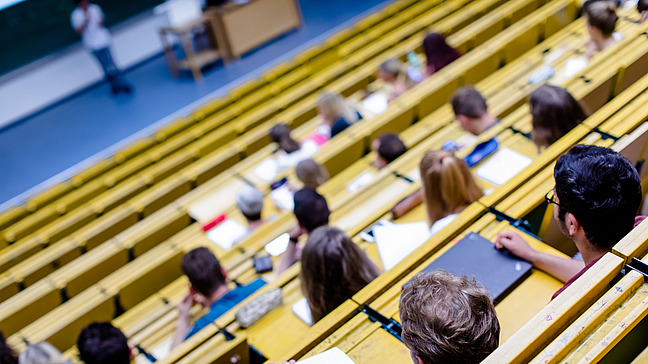 View from above of rows of seats in a lecture hall. The students are taking notes on their notepads.