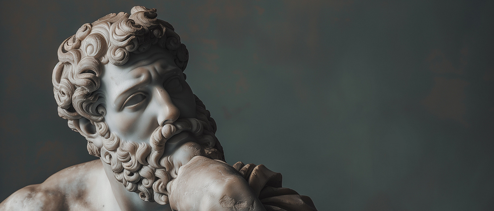 A detailed sculpture of a thoughtful male figure with curly hair and a beard. The statue features a muscular chest and rests its head on one hand. The background is blurred.