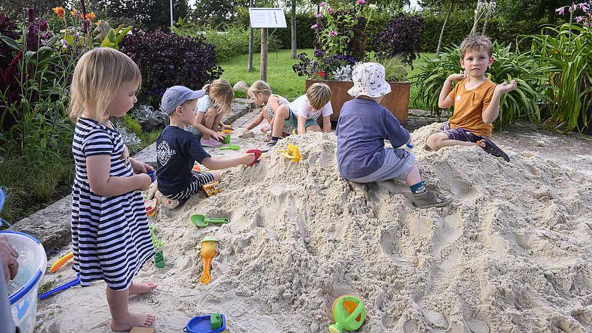 Several children are playing with sand toys in a large sandpit.