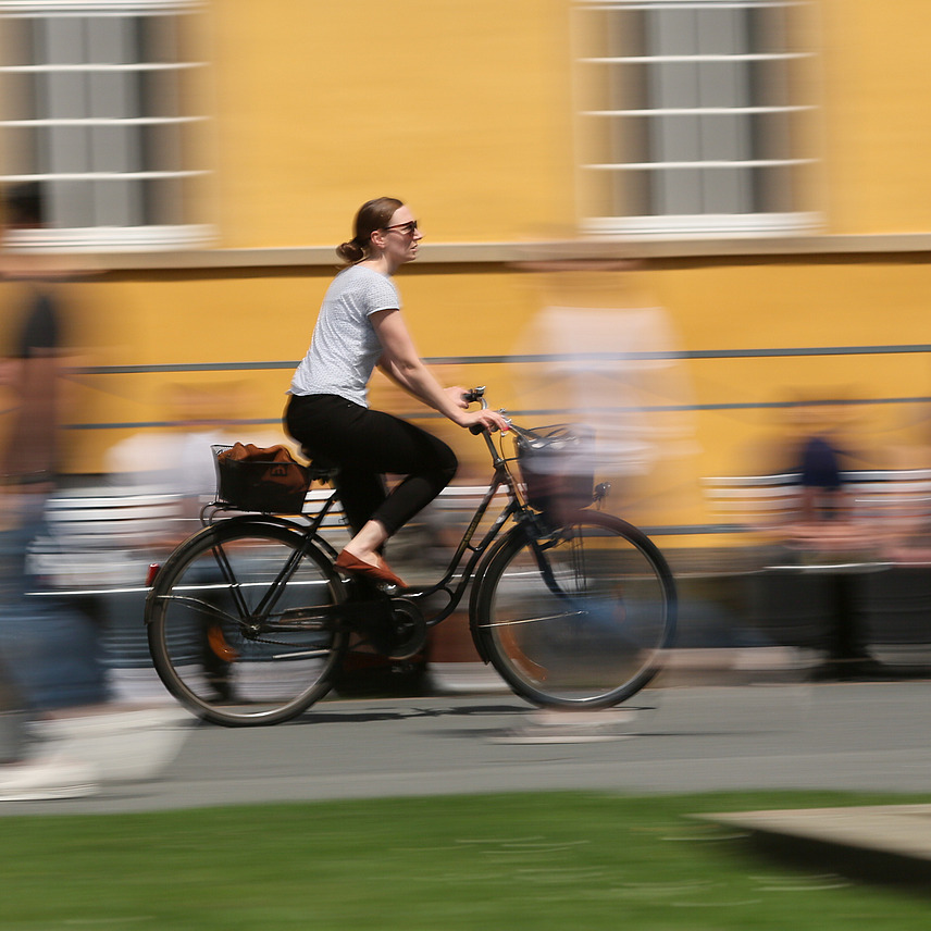 Bicyclist riding fast in front of Osnabrück Castle, photographed with motion blur.