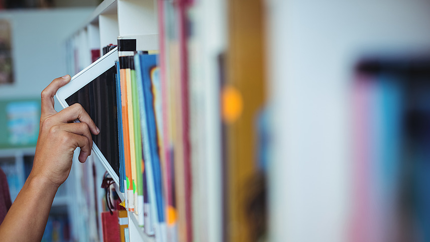 A book is placed by hand on a filled bookshelf.