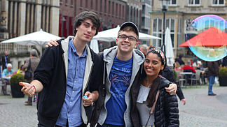 Drei internationale Studierende stehen lächelnd in der Bremer Innenstadt auf einem Marktplatz.