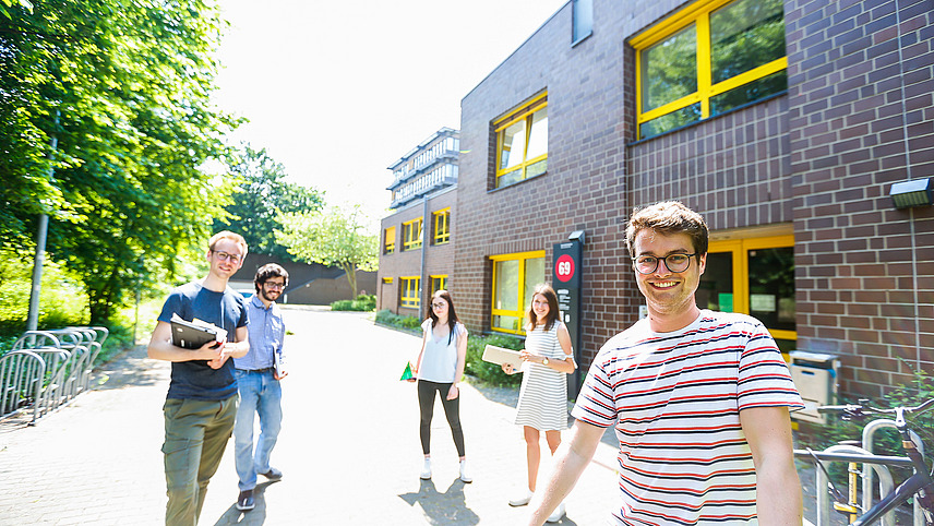 Fünf Studierende stehen bei gutem Wetter vor einem Backsteinhaus mit gelben Fenstern, das die Gebäudenummer 69 trägt. Dabei handelt es sich um das Mathematikgebäude der Universität.