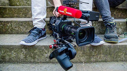 Detail of a man sitting on a staircase and holding a camera in his hand.