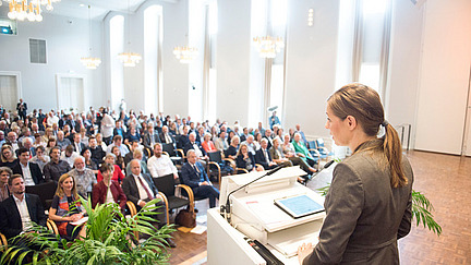 Prof. Dr. Susanne Menzel-Riedel speaks in front of an audience on a stage