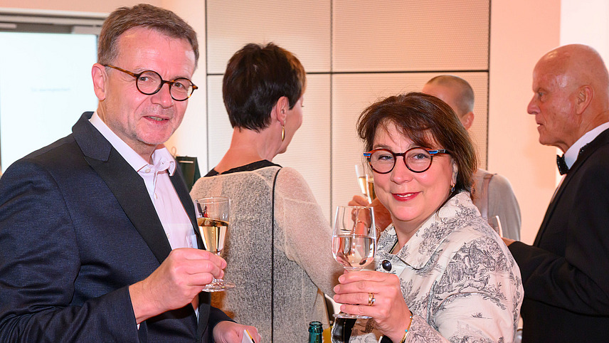 Two people with champagne glasses look into the camera