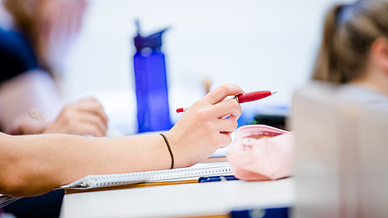 A person in a seat in a lecture hall. She is holding a ballpoint pen in her hand.