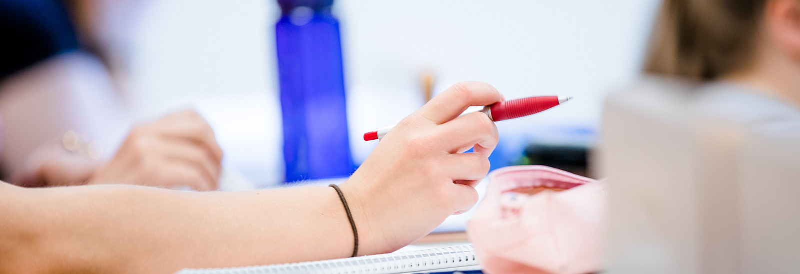 A person in a seat in a lecture hall. She is holding a ballpoint pen in her hand.