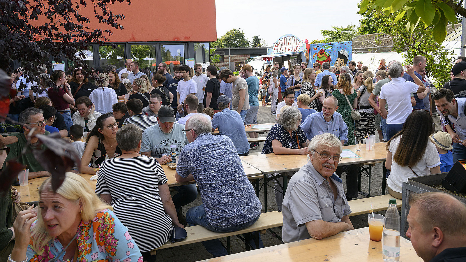 Numerous people are sitting on benches at tables at a party.