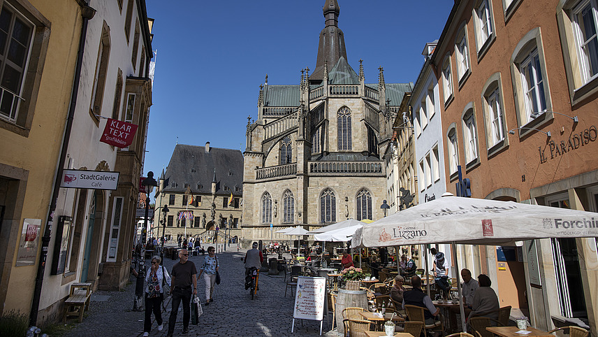 Blick auf die Sankt Marien Kirche und das Rathaus. Auf dem Platz haben einige Restaurants ihre Außenbereiche mit Sonnenschirmen und Sitzplätzen.