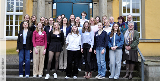 Eine Gruppe junger Frauen steht für ein Gruppenfoto vor einem großen gelben Gebäude