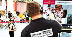 Eine Person invon hinten, auf dem T-Shirt ein Schriftzug des Instituts für Physik der Uni Osnabrück, im Hintergrund ein Kind mit VR-Brille