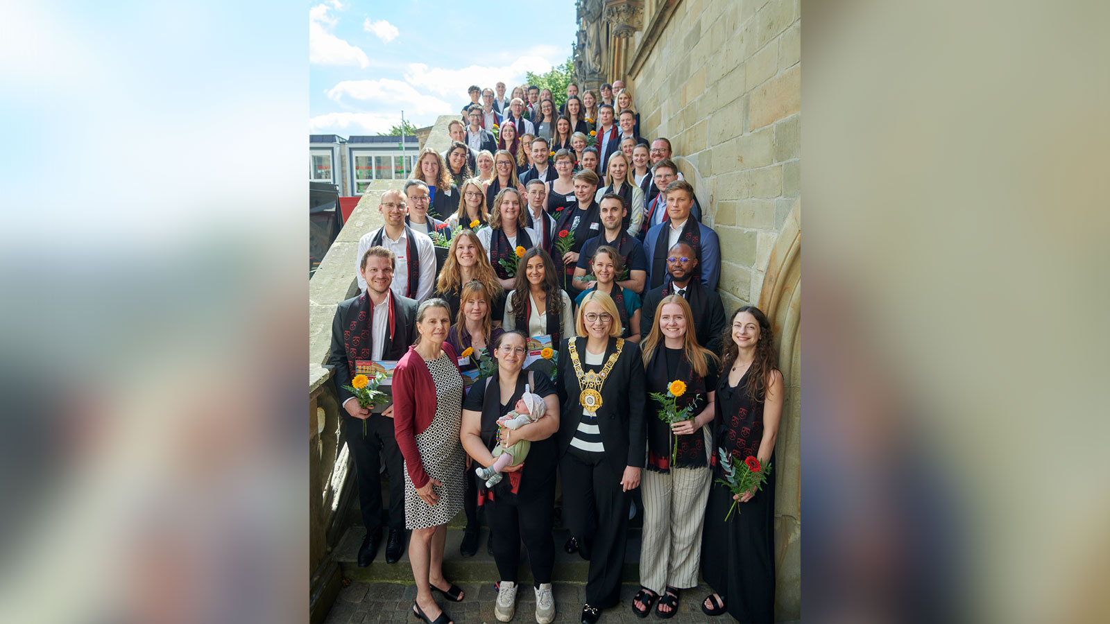 Eine Gruppe von festlich gekleideten Personen steht auf der Treppe eines historischen Gebäudes