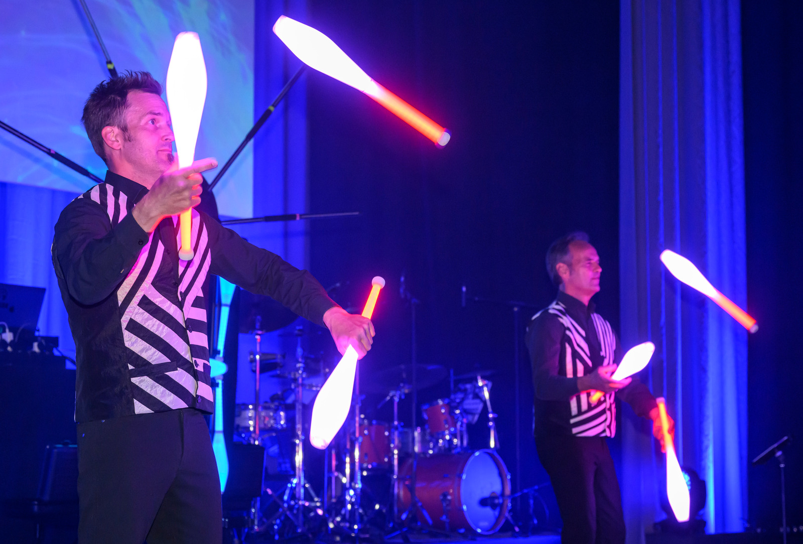 Two people juggle with glowing clubs